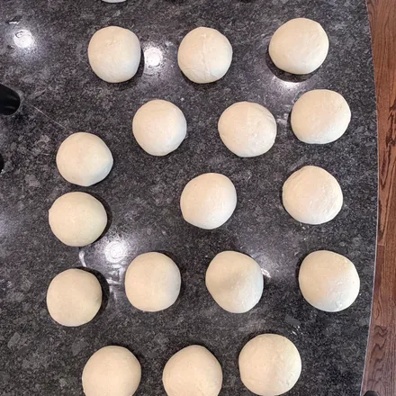 A batch of hand-portioned raw pizza dough balls resting on a granite counter