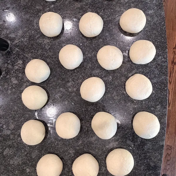 A batch of hand-portioned raw pizza dough balls resting on a granite counter