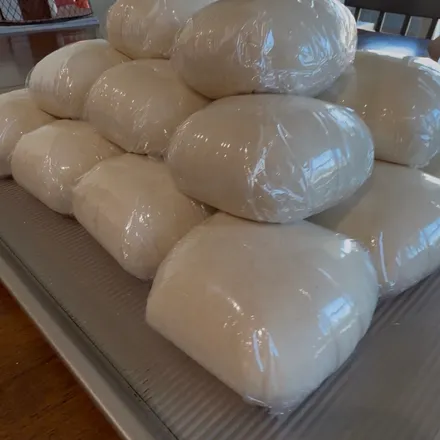 A stack of individually wrapped pizza dough balls on a sheet pan