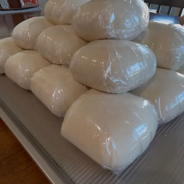 A stack of individually wrapped pizza dough balls on a sheet pan