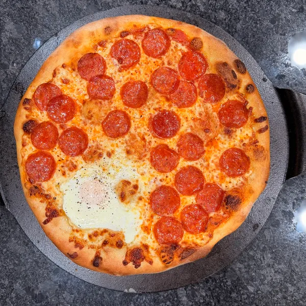 Rustic pepperoni pizza with a cracked egg baked into the center