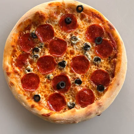 Pepperoni and black olive pizza with a golden puffed crust on a white board